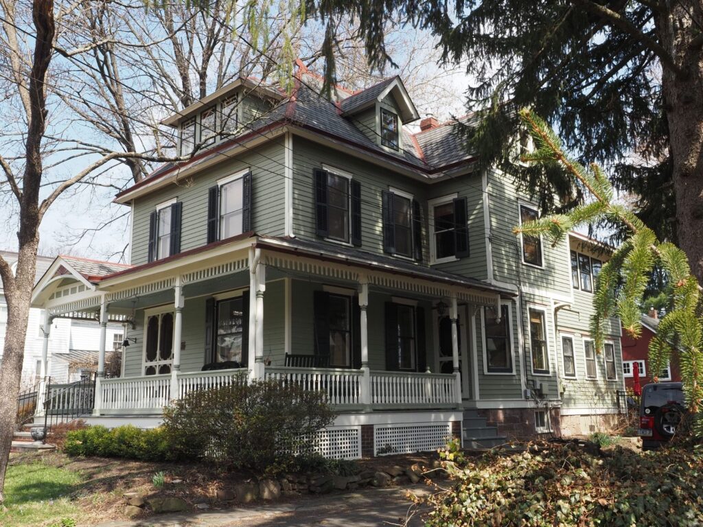 Historic Victorian-style house with a wraparound porch and mature trees in Newtown, Pennsylvania.